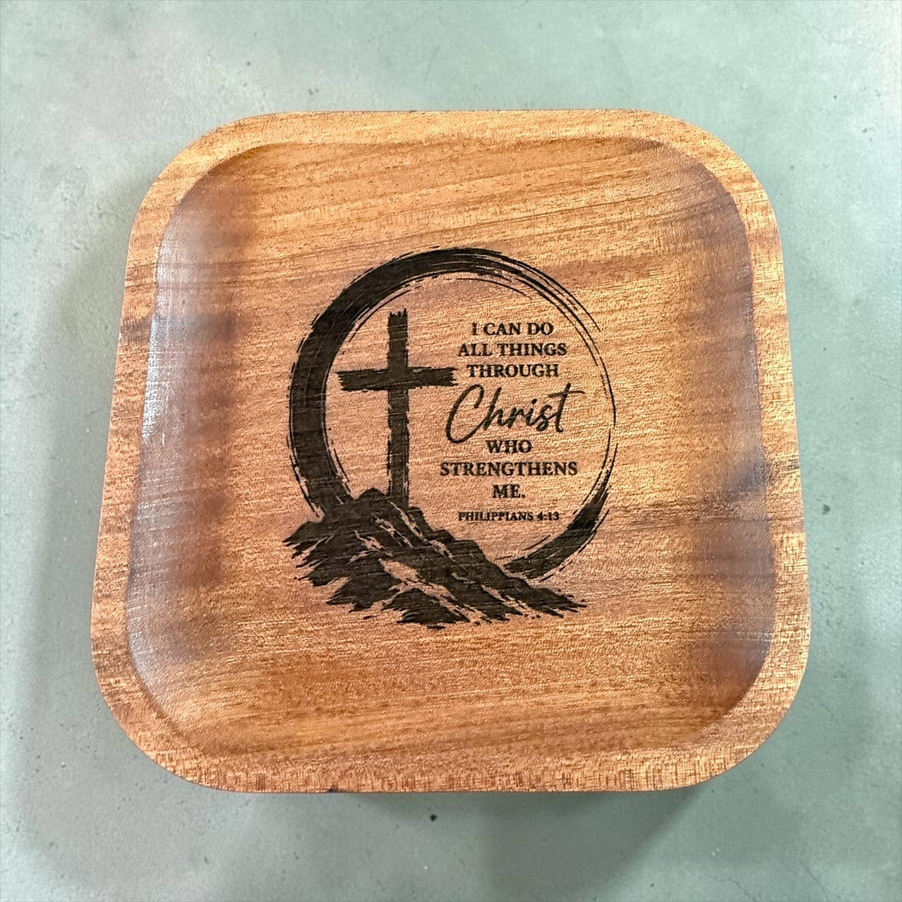 A square wooden tray with rounded corners, featuring a laser-engraved Christian design in the center with a cross, mountain silhouette, and the Bible verse Philippians 4:13: 'I CAN DO ALL THINGS THROUGH Christ WHO STRENGTHENS ME'.